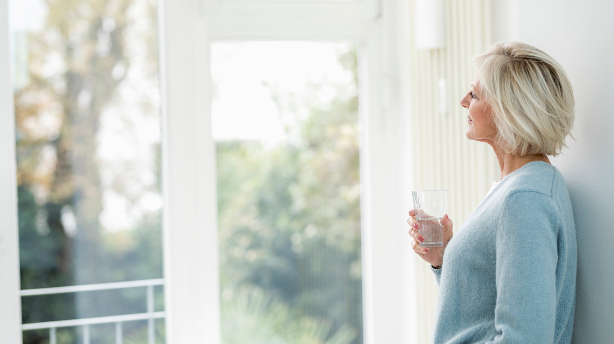 Vrouw drinkt glas water en kijkt naar buiten door het raam
