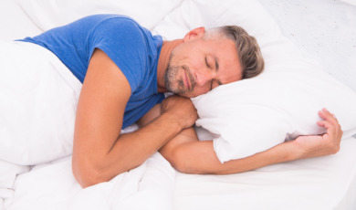 Man ligt op zijn linkerzij te slapen in een bed met wit beddengoed