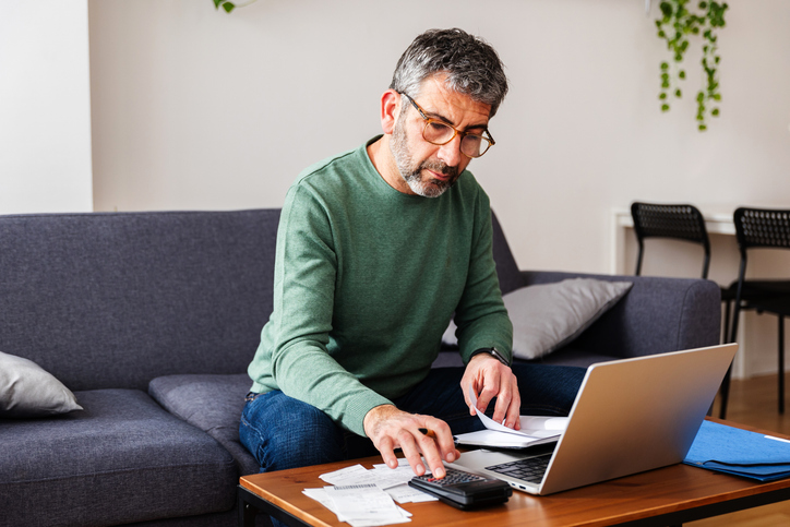 Man telt zijn geld in de woonkamer met laptop
