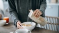 Vrouw schenkt sojamelk over cornflakes