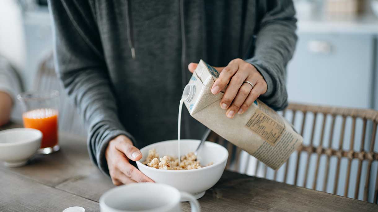 Vrouw schenkt sojamelk over cornflakes