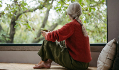 Vrouw zit gehurkt voor het raam naar buiten te staren