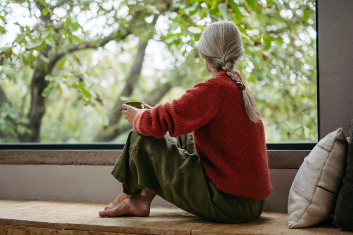 Vrouw zit gehurkt voor het raam naar buiten te staren