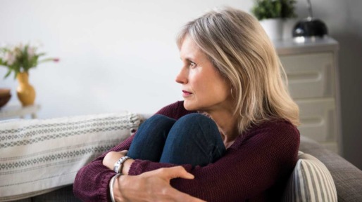 Vrouw zit op de bank en omarmt haar benen