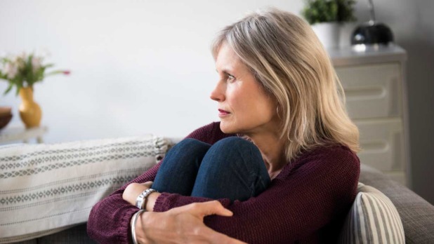 Vrouw zit op de bank en omarmt haar benen