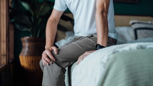Man met pijnlijke knie zit op bed
