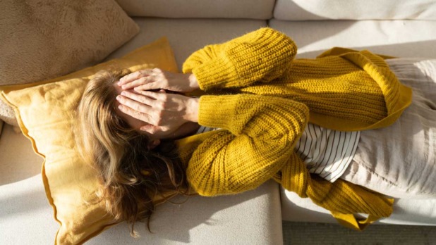 Vrouw met handen voor haar ogen ligt op de bank
