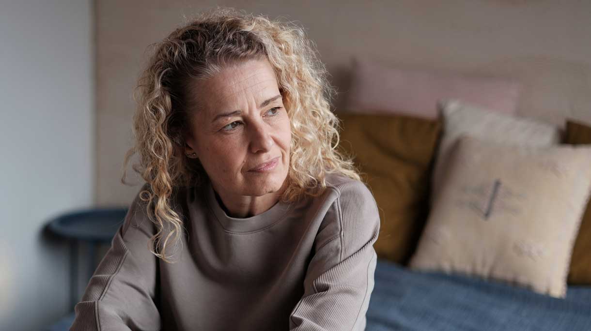 vrouw zit op bed kijkt met zorgelijke blik naar buiten