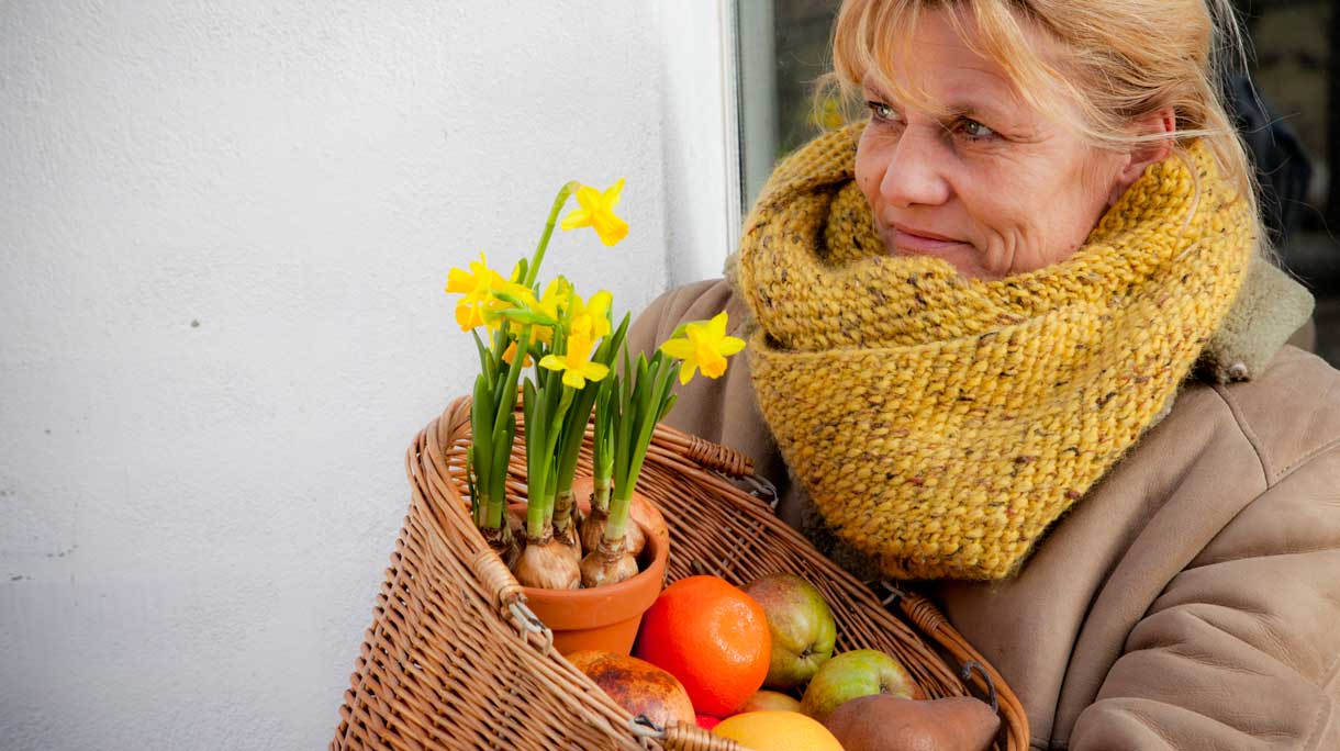 Vrouw met fruit en narcissen in een mand