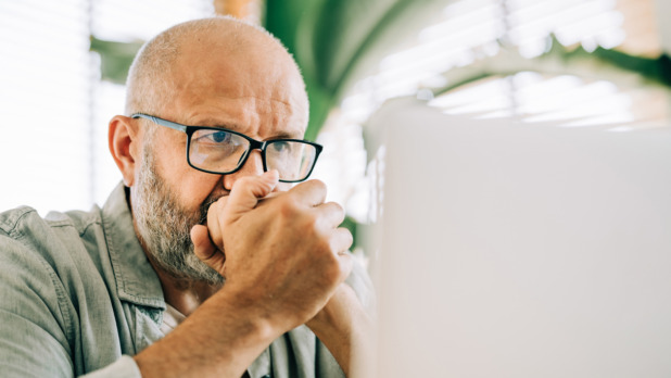 oudere man kijkt bezorgd naar laptop