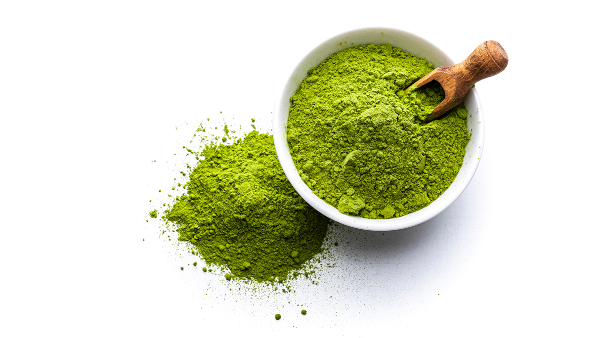 Matcha in een potje met een houten lepel op een witte achtergrond