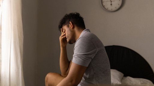 Man zit vermoeid op de rand van zijn bed na een slapeloze nacht