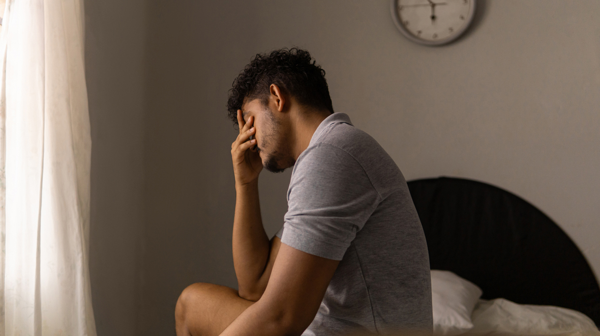Man zit vermoeid op de rand van zijn bed na een slapeloze nacht