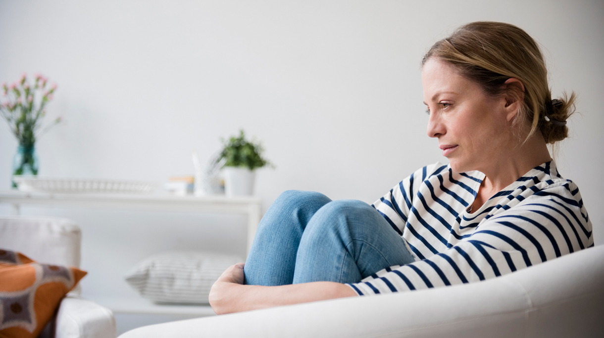 Vrouw zit op de bank thuis staart zorgelijk voor zich uit