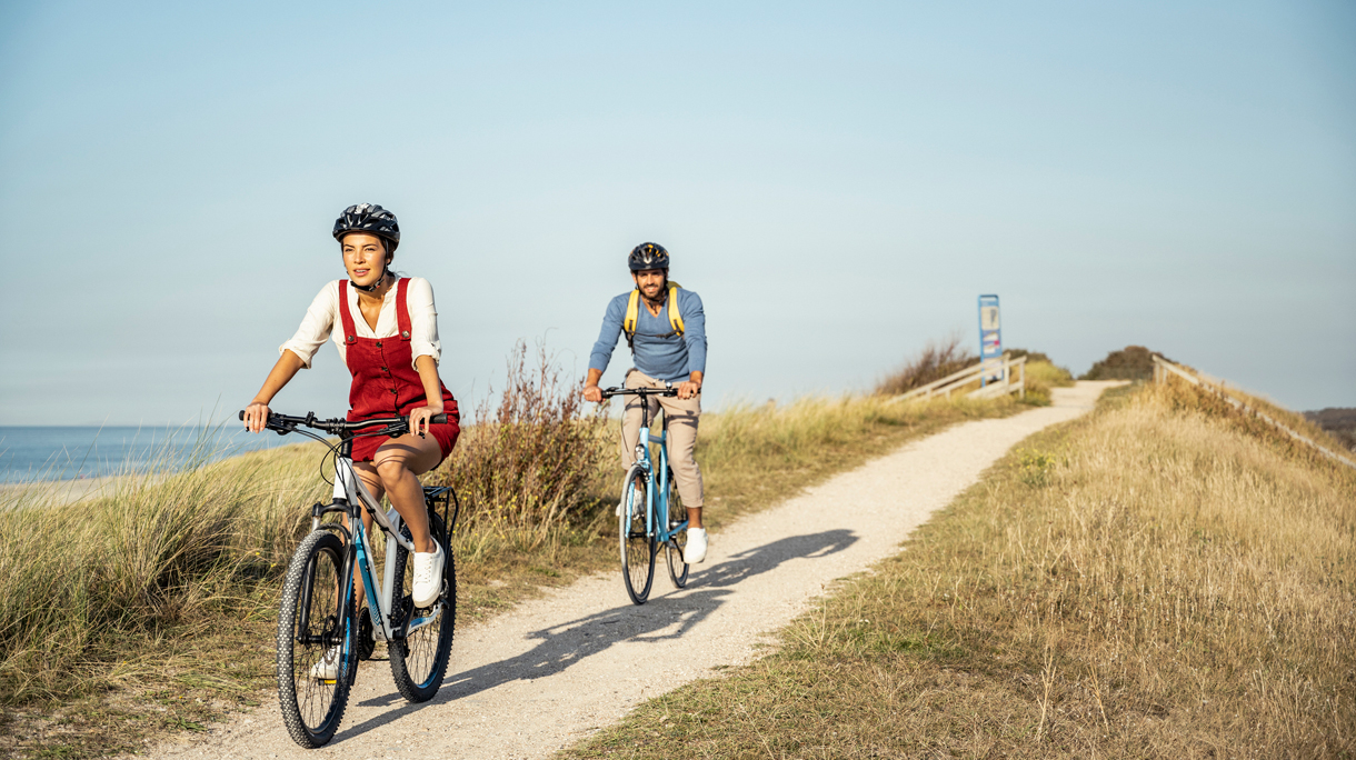 Man en vrouw fietsen in de duinen met fietshelm op