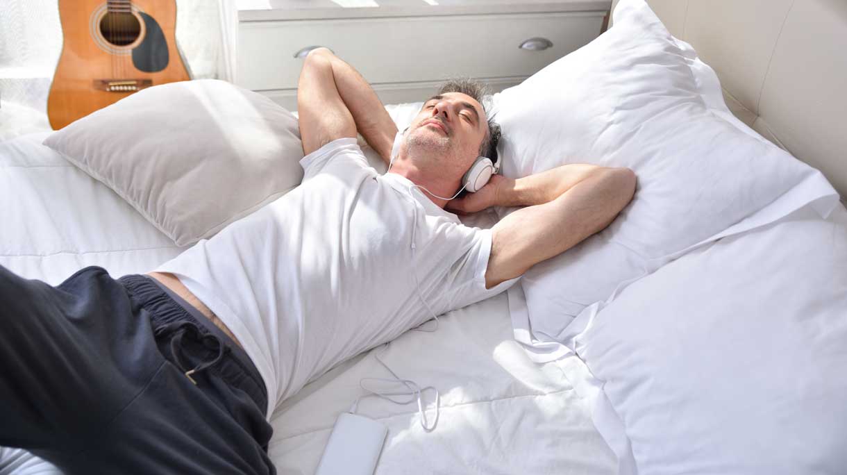 Man ligt op bed met koptelefoon