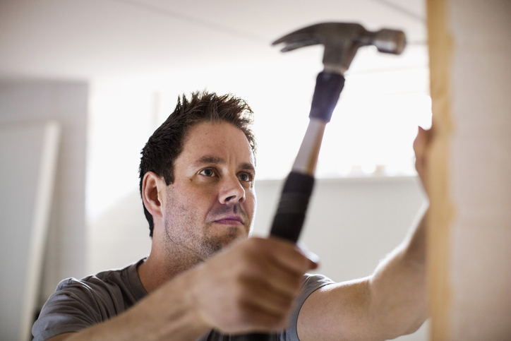 Klusser slaat met hamer spijkers in een muur