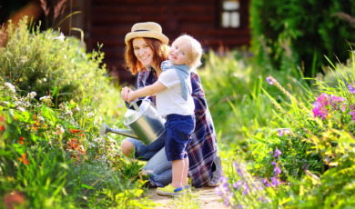 Toddler boy and his mother watering plants in the garden