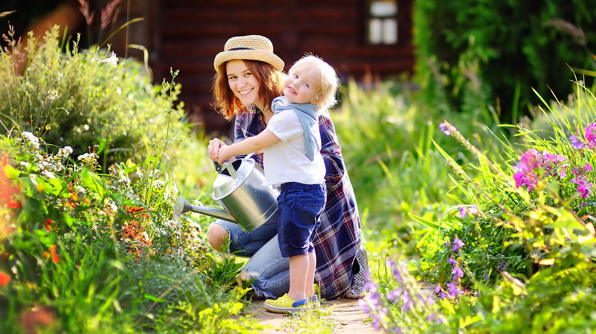 Toddler boy and his mother watering plants in the garden
