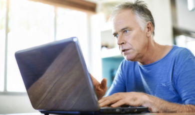 oudere man kijkt verschrikt op laptop