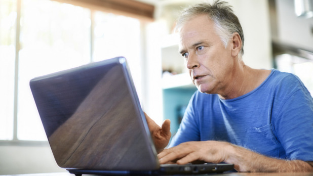 oudere man kijkt verschrikt op laptop