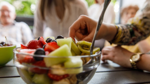 Vrouw eet stuk fruit uit een schaal met verschillende soorten fruit