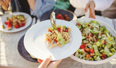 Vrouw schept pastasalade op bord op een mooie zomerse dag in de tuin