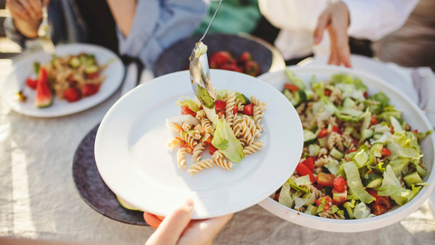 Vrouw schept pastasalade op bord op een mooie zomerse dag in de tuin