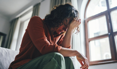 Vrouw zit zorgelijk op bed