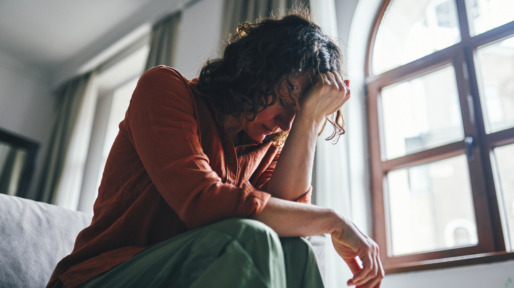 Vrouw zit zorgelijk op bed