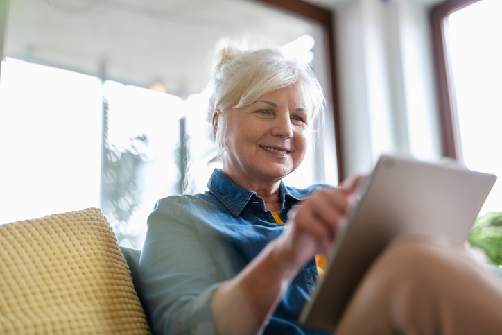 Vrouw zit vrolijk met tablet op de bank te swipen